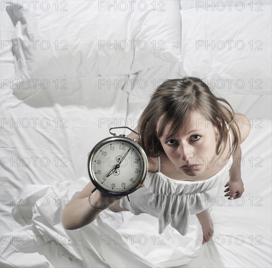 Hispanic woman holding alarm clock in bed