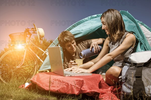 Couple drinking coffee and using laptop in camping tent