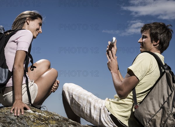 Man photographing woman on rock with cell phone