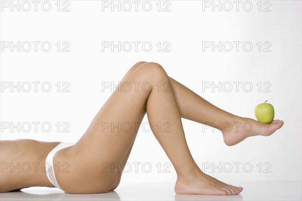 Caucasian woman lifting green apple with foot