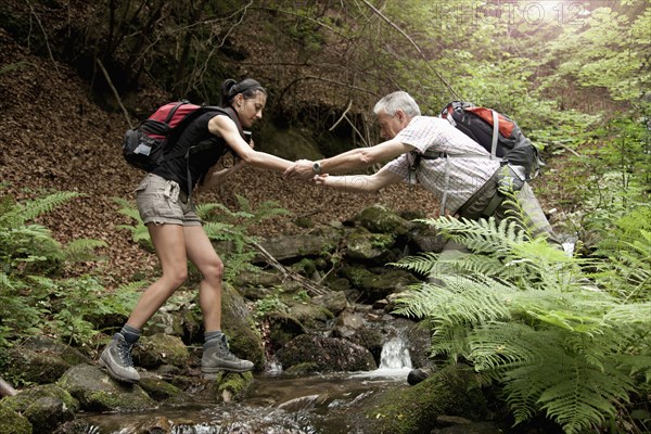 Caucasian man helping woman crossing forest river