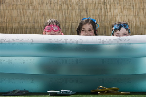 Smiling Caucasian children hiding in inflatable swimming pool