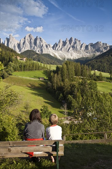 Mother and son sitting on bench admiring scenic view of mountains