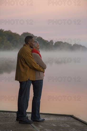 Older couple hugging at foggy river at sunrise