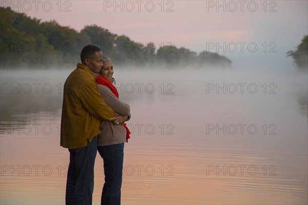 Older couple hugging at foggy river at sunrise