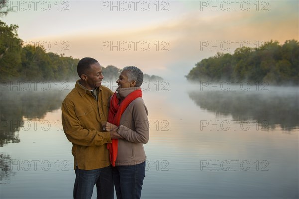 Older couple hugging at foggy river at sunrise