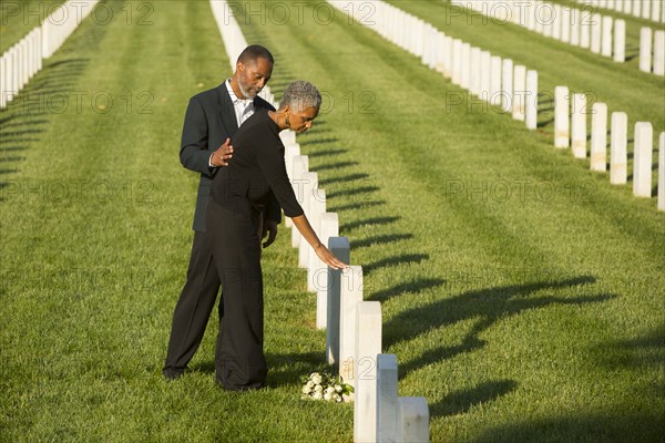 Black couple touching gravestone at military cemetery