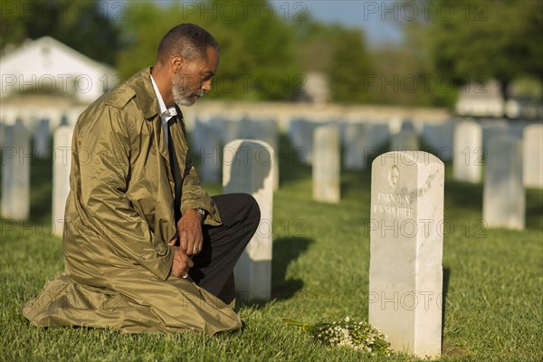 Black man kneeling with bouquet at military cemetery