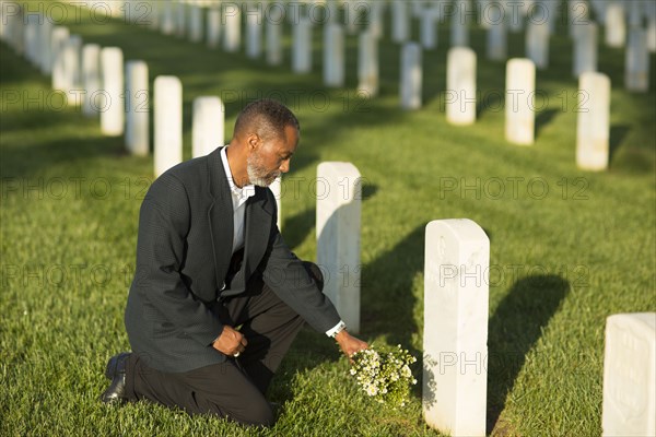 Black man kneeling with bouquet at military cemetery