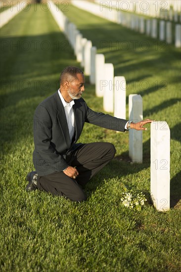 Black man kneeling with bouquet at military cemetery