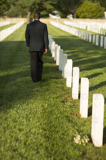 Black man leaving bouquet at gravestone at military cemetery