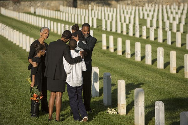Multi-generation Black family hugging in military cemetery