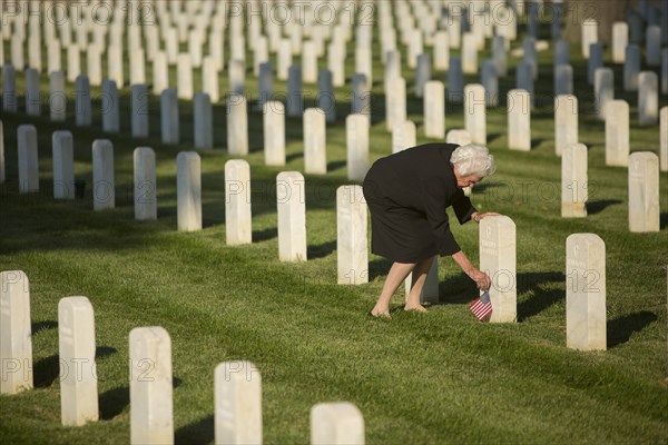 Caucasian widow placing American flag at cemetery gravestone