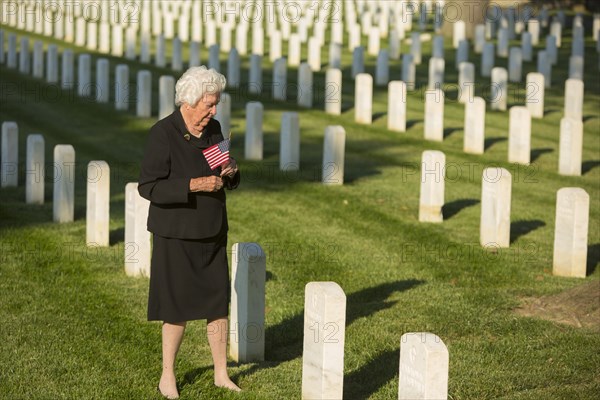 Caucasian widow holding American flag at cemetery gravestone