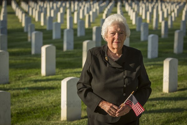 Caucasian widow holding American flag in cemetery