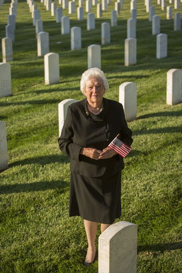 Caucasian widow holding American flag in cemetery