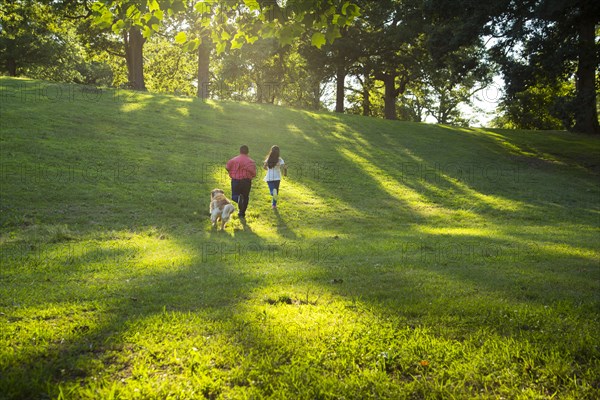 Hispanic brother and sister running with dog on hill