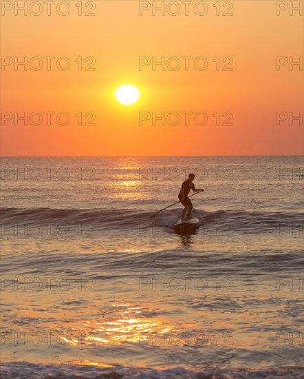 Silhouette of man paddleboarding on ocean waves