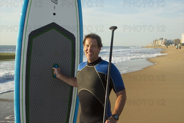 Man posing with paddleboard on beach