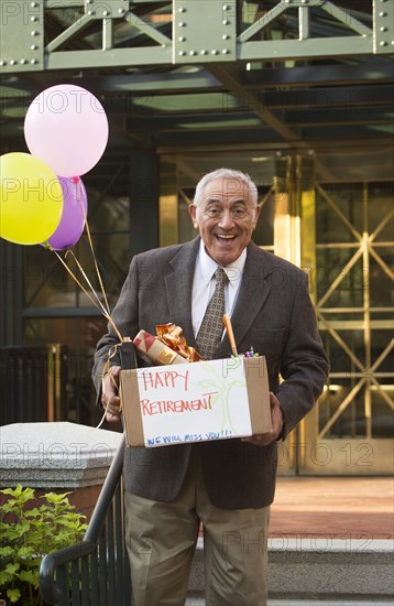 Hispanic man carrying belongings with happy retirement sign and balloons