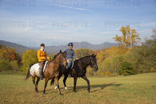 Older Caucasian couple horseback riding in field