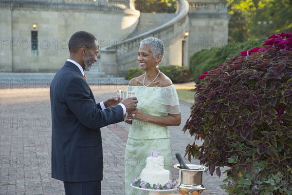 Black couple drinking champagne near wedding cake