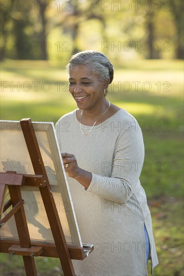 Black woman painting on canvas in park