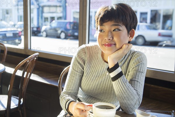 Pensive Asian teenage girl drinking coffee in coffee shop