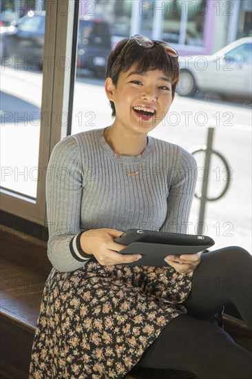 Asian teenage girl using digital tablet on window sill