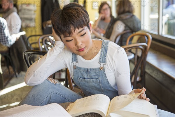 Asian teenage girl reading book in coffee shop