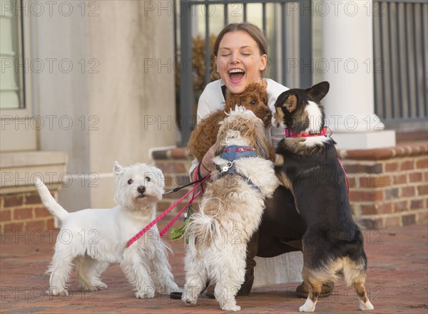 Caucasian woman playing with dogs on city sidewalk