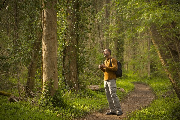 African American man standing on path in forest holding binoculars