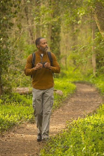 African American man walking on path in forest holding binoculars