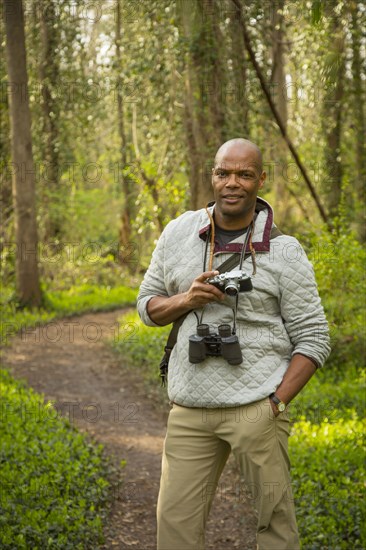 African American man standing on path in forest holding camera