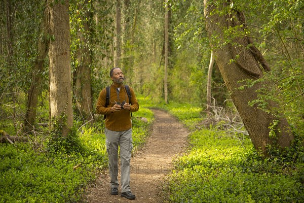 African American man walking on path in forest holding binoculars