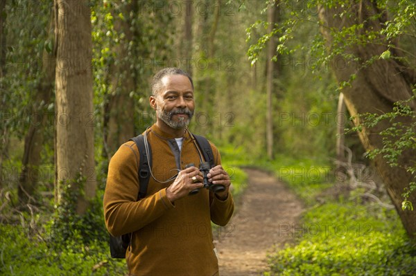 African American man standing on path in forest holding binoculars