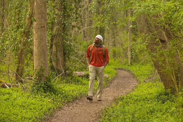 African American man walking on path in forest carrying backpack