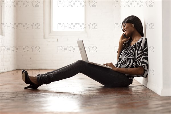 African woman using laptop and talking on cell phone in empty room