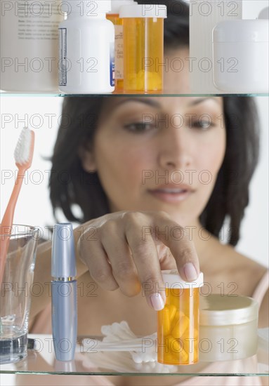 Young woman taking pills out of medicine cabinet