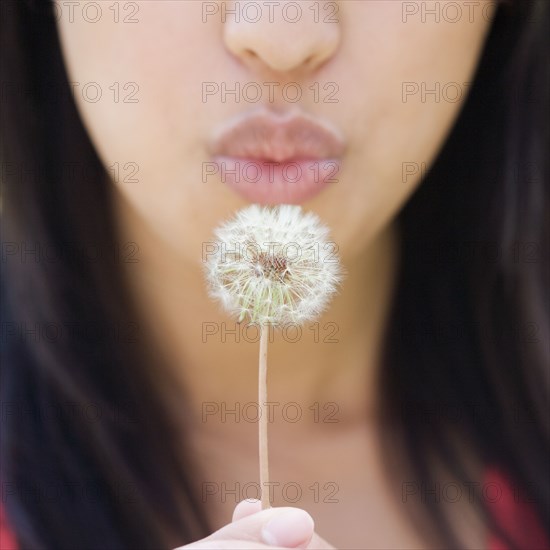 Close up of lower half of woman's face blowing dandelion