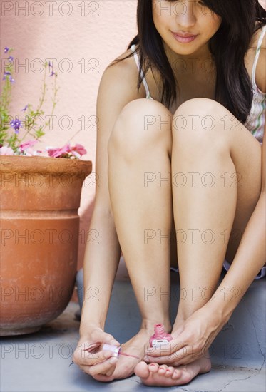 Woman sitting on stairs painting toenails