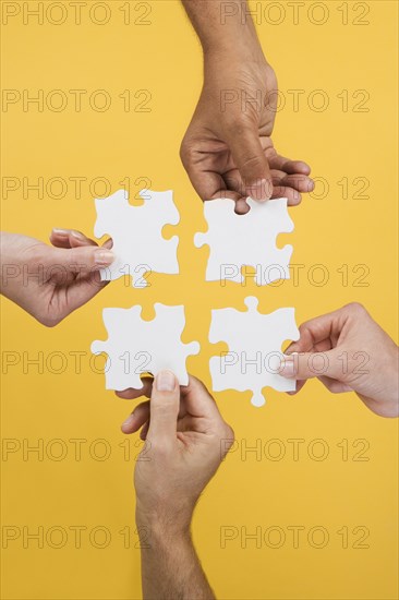 Close up of four hands holding puzzle pieces