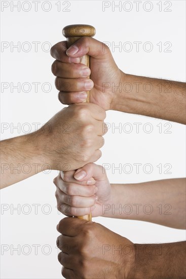 Close up of four hands holding baseball bat