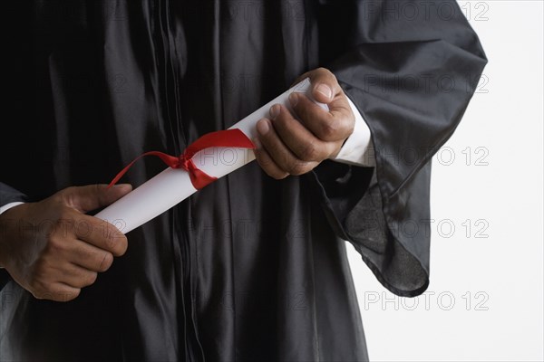 Mid section of man in graduation gown holding diploma