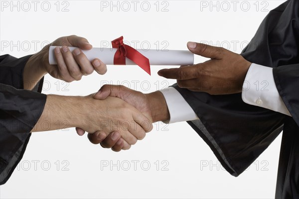 Close up of man's hands receiving diploma in graduation gown