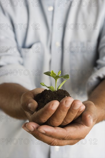 Close up of hands holding mound of dirt and plant