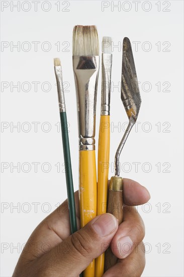 Close up of hands holding paintbrushes and palette knife