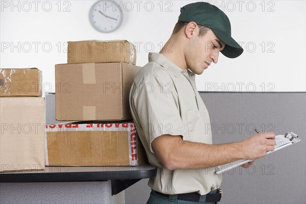 Profile of delivery man writing in clipboard with stack of boxes behind him