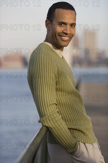 Portrait of man leaning against bridge with city behind him