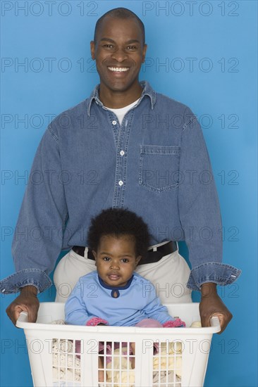 Father doing laundry with baby daughter in hamper